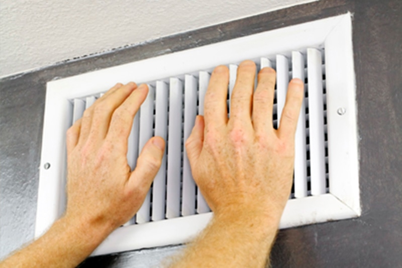 Air conditioner blowing hot air. Hands over air conditioning vent feeling for air flow.