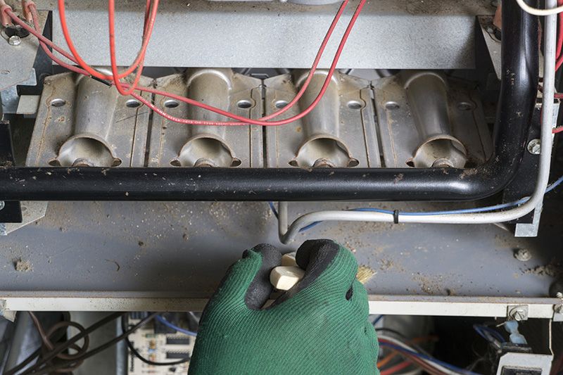 Image of someone servicing a furnace using green gloves.