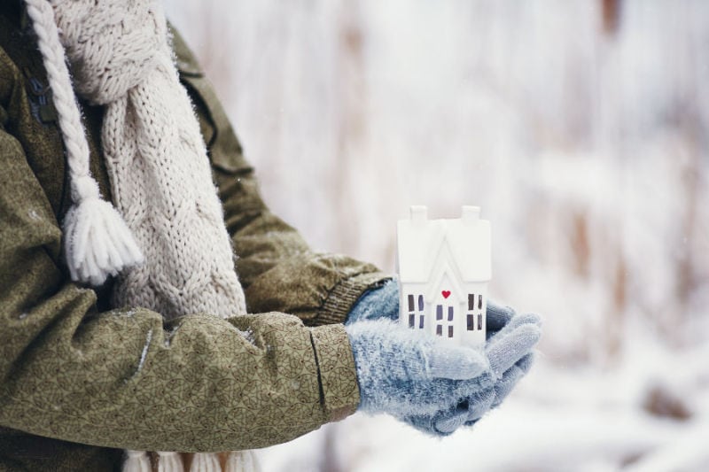 House in gloved hands during winter. Person considering heat load calculation for HVAC equipment. Reliant Heating & Cooling blog image.